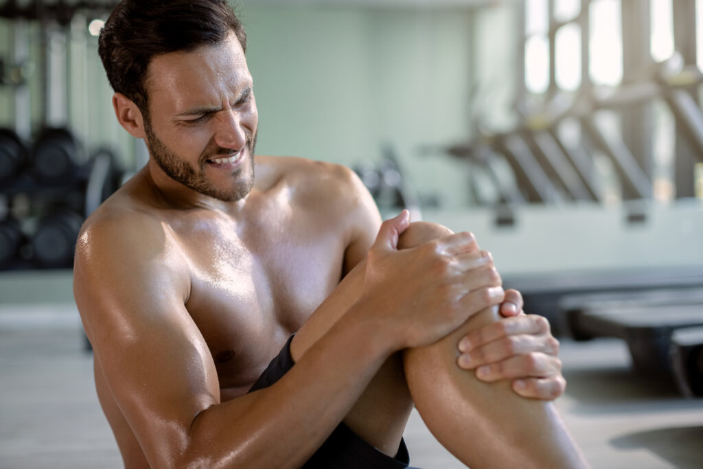 Male athlete holding his knee in pain while working out in a gym