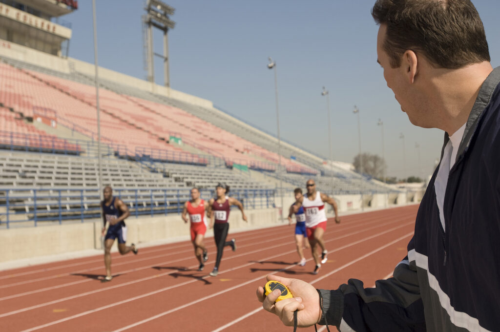 Male trainer measuring time while athletes racing